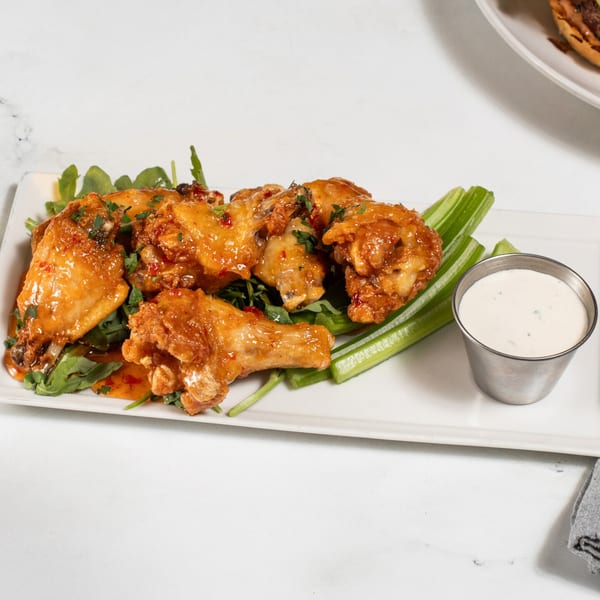 Sweet chili chicken wings with celery sticks and ranch dressing on a white rectangular plate.