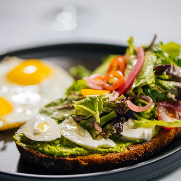 Avocado toast with mozzarella, salad, and a fried egg on a black plate.