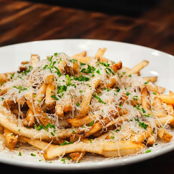 A white plate piled high with golden french fries, topped with grated cheese and fresh parsley.