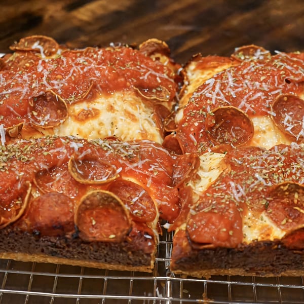 Close-up of two square slices of CROCCANTE ARTISAN PIZZA with pepperoni, cheese, and herbs.