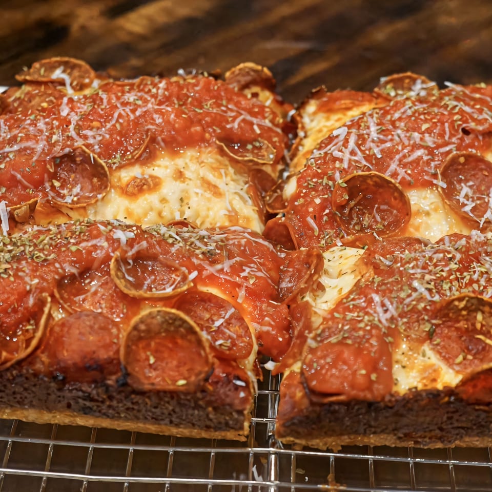 Close-up of two square slices of CROCCANTE ARTISAN PIZZA with pepperoni, cheese, and herbs.