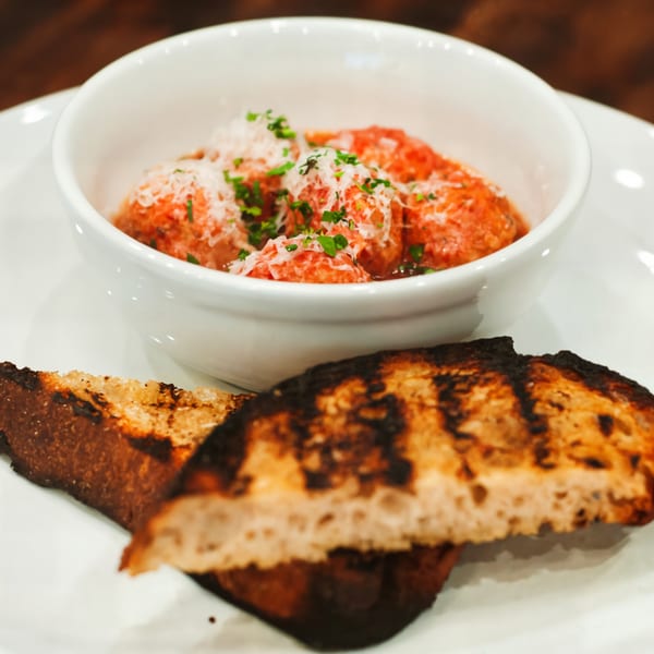 Meatballs in red sauce topped with parmesan and parsley, served with grilled bread.
