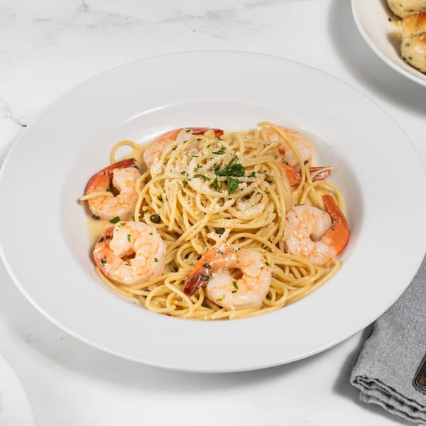 Spaghetti with shrimp, capers, and parsley, topped with grated cheese in a white bowl.