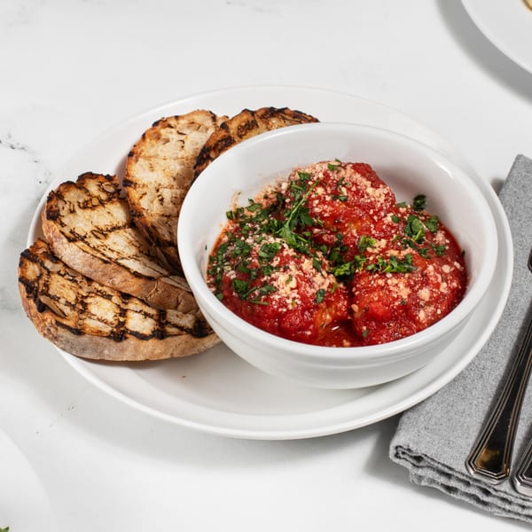 Meatballs in red sauce with parmesan and parsley, served with grilled bread on a white plate.