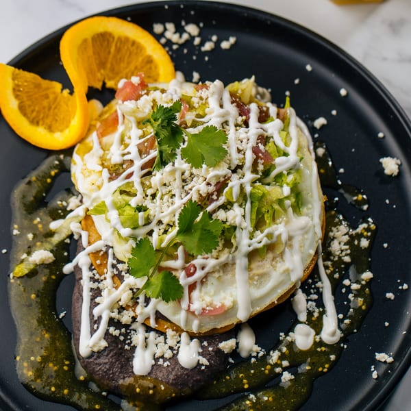 Huevos rancheros with black beans, green salsa, sour cream, cheese, and orange slices.