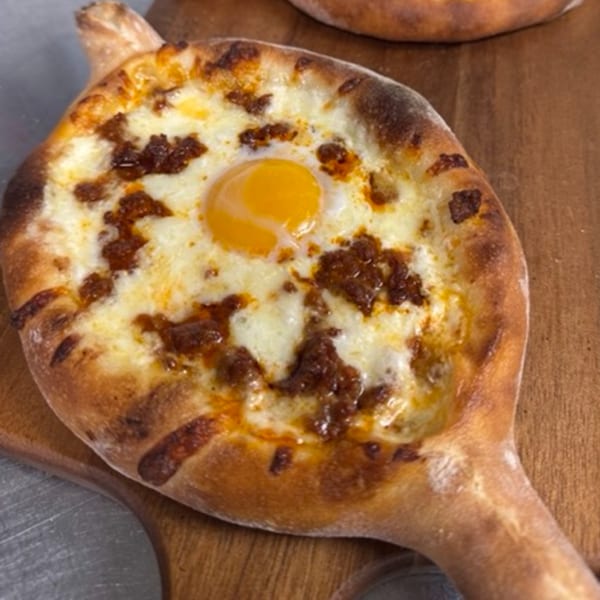 CROCCANTE ARTISAN PIZZA's boat-shaped pizza with melted cheese, spicy sausage, and a sunny-side-up egg.