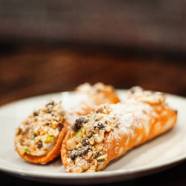 Three cannoli pastries filled with cream, topped with nuts, chocolate chips, and powdered sugar.