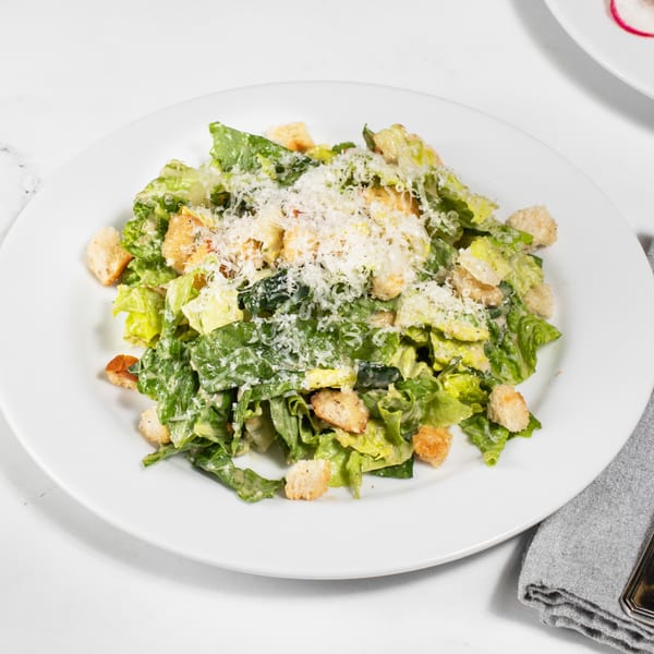 A Caesar salad with romaine lettuce, croutons, and grated Parmesan cheese on a white plate.