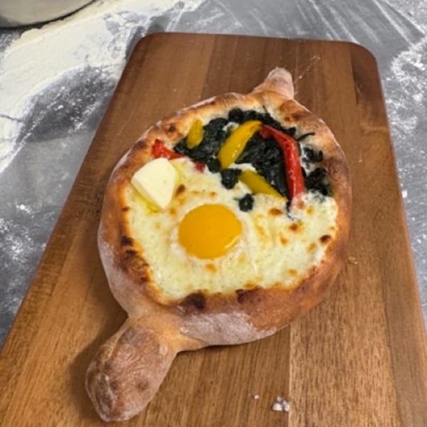 Boat-shaped pizza with a runny egg yolk, melted cheese, spinach, and bell peppers on a wooden board.