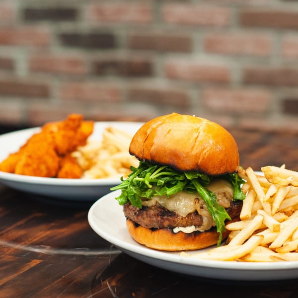 A gourmet burger with arugula and cheese, served with fries, and chicken tenders in the background.