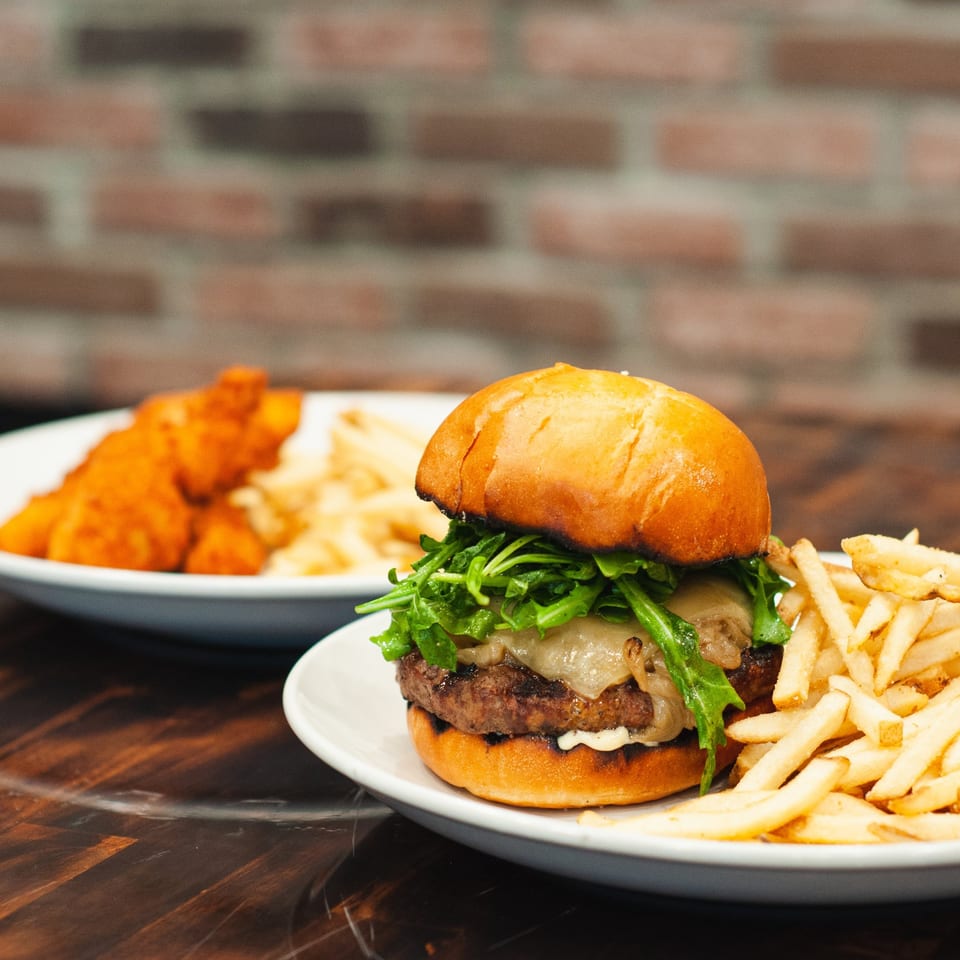 A gourmet burger with arugula and cheese, served with fries, and chicken tenders in the background.