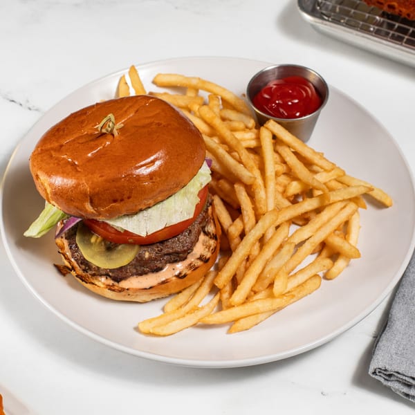 A beef burger with lettuce, tomato, and pickles, served with golden fries and ketchup.